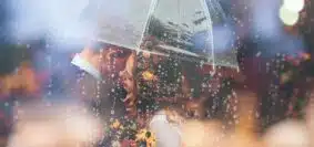 a bride and groom kiss in the rain under an umbrella